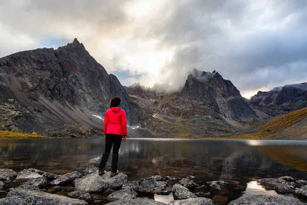 Mulher em pé em uma rocha em um lago alpino cercado por montanhas acidentadas — Fotografia de Stock