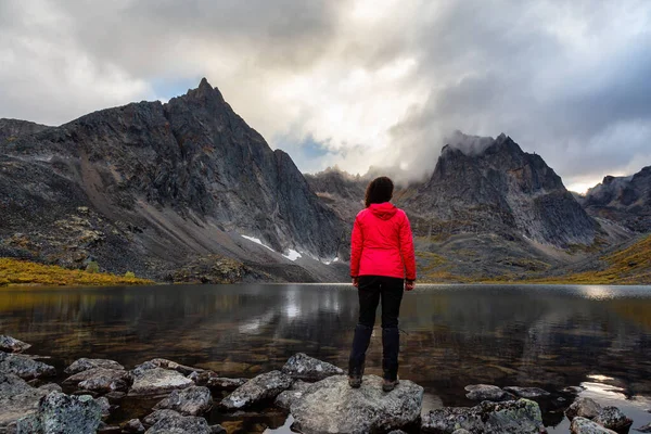 Mulher em pé em uma rocha em um lago alpino cercado por montanhas acidentadas — Fotografia de Stock
