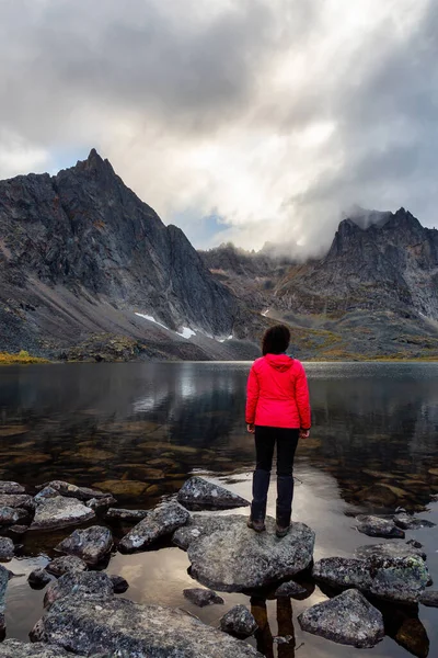 Mulher em pé em uma rocha em um lago alpino cercado por montanhas acidentadas — Fotografia de Stock