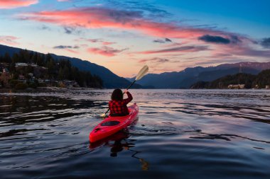 Parlak kırmızı bir kanoda kürek çeken maceraperest kız.