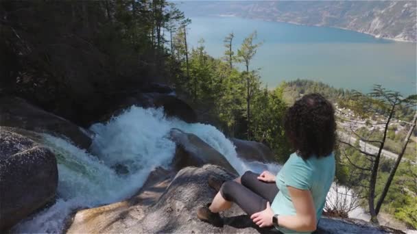 Dobrodružná dospělá žena sedí na vrcholu krásného vodopádu — Stock video