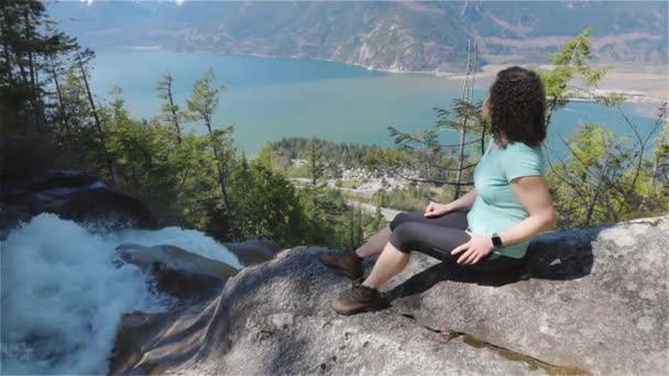 Adventurous Adult Woman est assis sur le dessus d'une belle cascade — Video