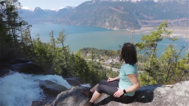 Äventyrlig vuxen kvinna sitter på toppen av ett vackert vattenfall — Stockvideo