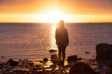Maceracı Kafkas Yetişkin Kadın Batı Sahili Pasifik Okyanusu 'ndaki kayalık bir sahilde dramatik bir Sunset izliyor. White Rock, Greater Vancouver, British Columbia, Kanada.