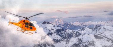 Sarı helikopter Rocky Dağları üzerinde uçuyor.