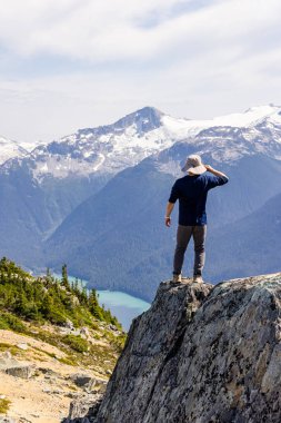 Bir insan dağlarla çevrili bir kayanın üzerinde duruyor ve Whistler 'da mavi bir göl..