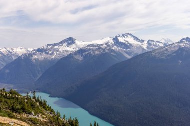 Pırıl pırıl bir göl, karla kaplı tepeler ve Whistler, BC 'deki yemyeşil ormanlardan oluşan güzel bir manzara..