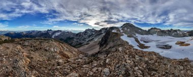 Kanada, BC 'nin engebeli dağ zirveleri ve buzulları, nefes kesen bulutlu gökyüzünün altında..