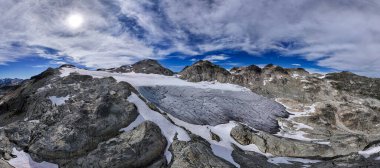 Kanada, BC 'de güneşli bir gökyüzünün altında kayalık dağlarla çevrili görkemli buzullar..