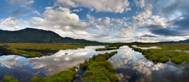 Sulak alanlar, dingin Kanada manzarasındaki tepelerle çevrili canlı bir gökyüzünü yansıtıyor..