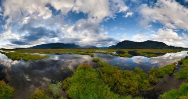 Kanada, BC 'de aynadan yansıyan sular ve dramatik bulutlarla sakin bir bataklık..