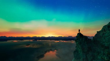 Gün batımında zirvede duran bir yürüyüşçünün silueti..