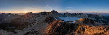 BC, Kanada 'da canlı bir gündoğumu altında dağların ve buzulların panoramik manzarası.