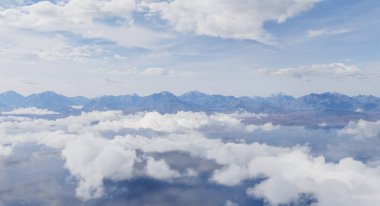 Karlı dağların, bulutların ve mavi gökyüzünün yer aldığı çarpıcı bir sahne..