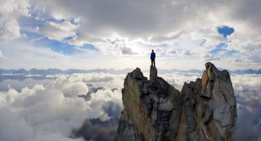 Sabah gökyüzünün altındaki bulutlarla çevrili bir dağın tepesinde tek başına duruyor.