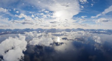 Etrafı dağlarla çevrili yansıtıcı göl, bulutlar ve dingin manzarada parlak gökyüzü..