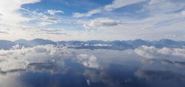 Yansıtıcı göl ve gerçekçi 3 boyutlu bulutlarla sakin dağ manzarası.