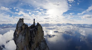 Uçsuz bucaksız gökyüzü ve sakin su yansımalarıyla kayalık bir zirvenin tepesinde tek bir figür..