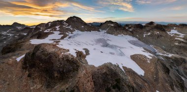 Britanya Kolumbiyası, Kanada, Alp Dağları 'ndaki sivri kayalık tepeler ve kar tarlaları üzerinde dramatik gün batımı.