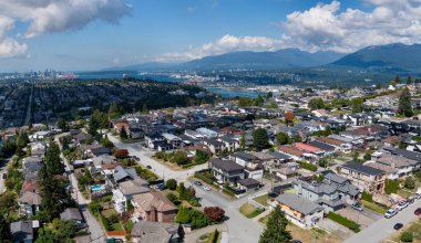Burnaby, Greater Vancouver, BC, Kanada; yüksek bir bakış açısına sahip evler, sokaklar, ağaçlar ve uzak dağlardan görülen banliyö yerleşim yerleri.
