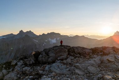 Kırmızı ceketli yalnız bir yürüyüşçü Kanada 'daki British Columbia' da gün doğumunda engebeli tepelere bakar..