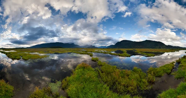 Kanada, BC 'de aynadan yansıyan sular ve dramatik bulutlarla sakin bir bataklık..