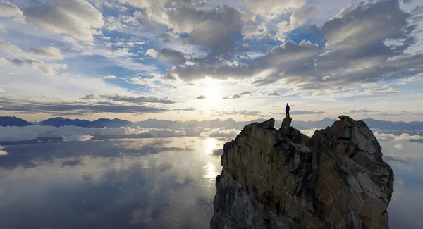 Bir insan uçurumun tepesinde durur, nefes kesici bir dağ ve su manzarasıyla..