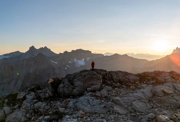 Kırmızı ceketli yalnız bir yürüyüşçü Kanada 'daki British Columbia' da gün doğumunda engebeli tepelere bakar..