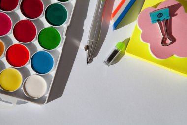 beyaz bir masa üzerinde renk boyaları, kalem, silgi, kağıt ve makas.