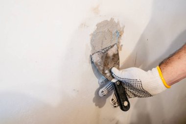 Bir işçinin elinin, kalın yama bileşenine veya iç duvarın hasarlı bir bölümüne sıkıca bastırmak için küçük bir macun bıçağı kullanarak yakın plan görüntüsü..