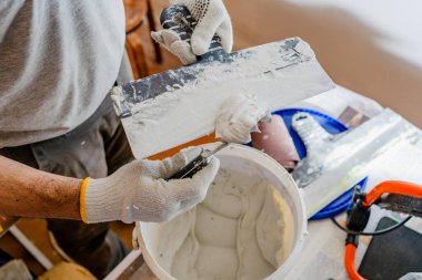 Ağır, beyaz, ıslak eklem birleşimi bir kovadan geniş, profesyonel bir malanın yüzeyine aktarılır..