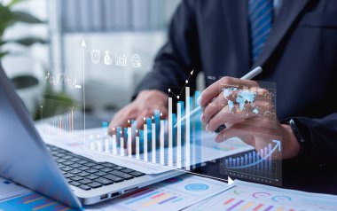 Finans ve iş büyüme grafiklerini karşılaştırmak için dizüstü bilgisayar kullanan işadamı, gelecek yılın performansını tahmin etmek, yatırım planlamasına rehberlik etmek ve maliyet azaltma hedeflerini desteklemek.