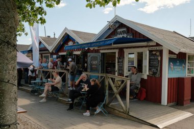 Nynashamn, Stockholm İlçesi, İsveç - 29 Mayıs 2025: Bir grup insan kırmızı bir binanın önünde bir dondurma dükkanının önünde oturuyorlar. Binanın üzerinde mavi bir tabela var.