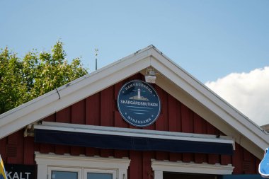 Nynashamn, Stockholm İlçesi, İsveç - 29 Mayıs 2025: Üzerinde beyaz harflerle Skargardsbutiken yazan kırmızı bir bina. Binanın beyaz bir süsü ve mavi bir tentesi var. İşaret dairesel.