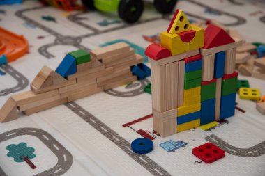 Neşeli oyun zamanı çocuğu, parlak dağınık odadaki oyuncak bloklardan kaleler yaratıyor, tasasız çocukluğun sembolü.