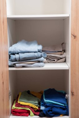 Dolabın raflarında düzgünce katlanmış giysiler var.