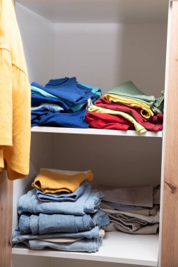 Dolabın raflarında düzgünce katlanmış giysiler var.