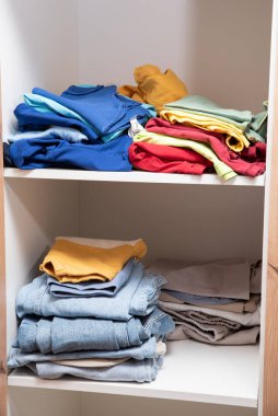 Dolabın raflarında düzgünce katlanmış giysiler var.