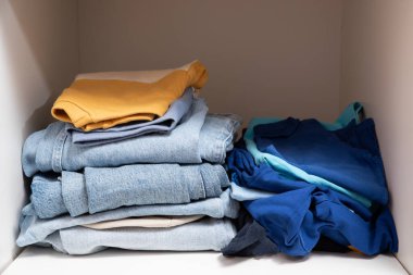 Dolabın raflarında düzgünce katlanmış giysiler var.