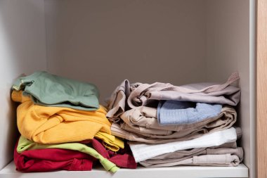 Dolabın raflarında düzgünce katlanmış giysiler var.