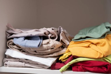 Dolabın raflarında düzgünce katlanmış giysiler var.