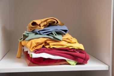 Dolabın raflarında düzgünce katlanmış giysiler var.