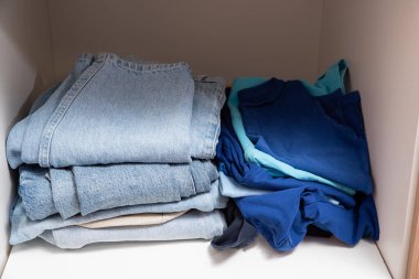 Dolabın raflarında düzgünce katlanmış giysiler var.