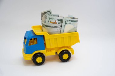 Dolar banknotları beyaz arka planda sarı ve mavi bir oyuncak arabayla taşınır..