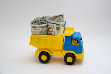 Dolar banknotları beyaz arka planda sarı ve mavi bir oyuncak arabayla taşınır..