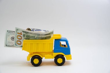 Dolar banknotları beyaz arka planda sarı ve mavi bir oyuncak arabayla taşınır..