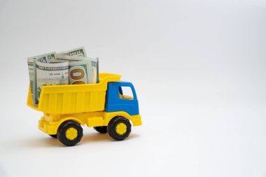 Dolar banknotları beyaz arka planda sarı ve mavi bir oyuncak arabayla taşınır..