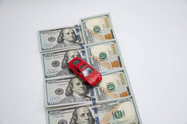 Kırmızı oyuncak araba beyaz arka planda dolar banknotlarıyla gidiyor. Araba sigortası