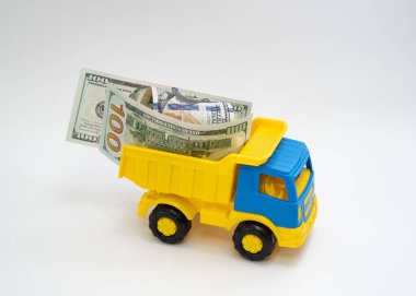 Dolar banknotları beyaz arka planda sarı ve mavi bir oyuncak arabayla taşınır..