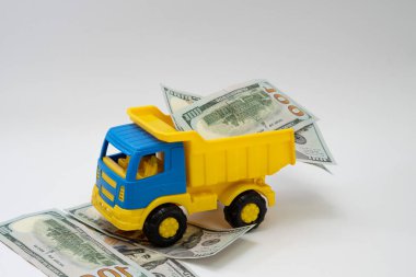Dolar banknotları beyaz arka planda sarı ve mavi bir oyuncak arabayla taşınır..